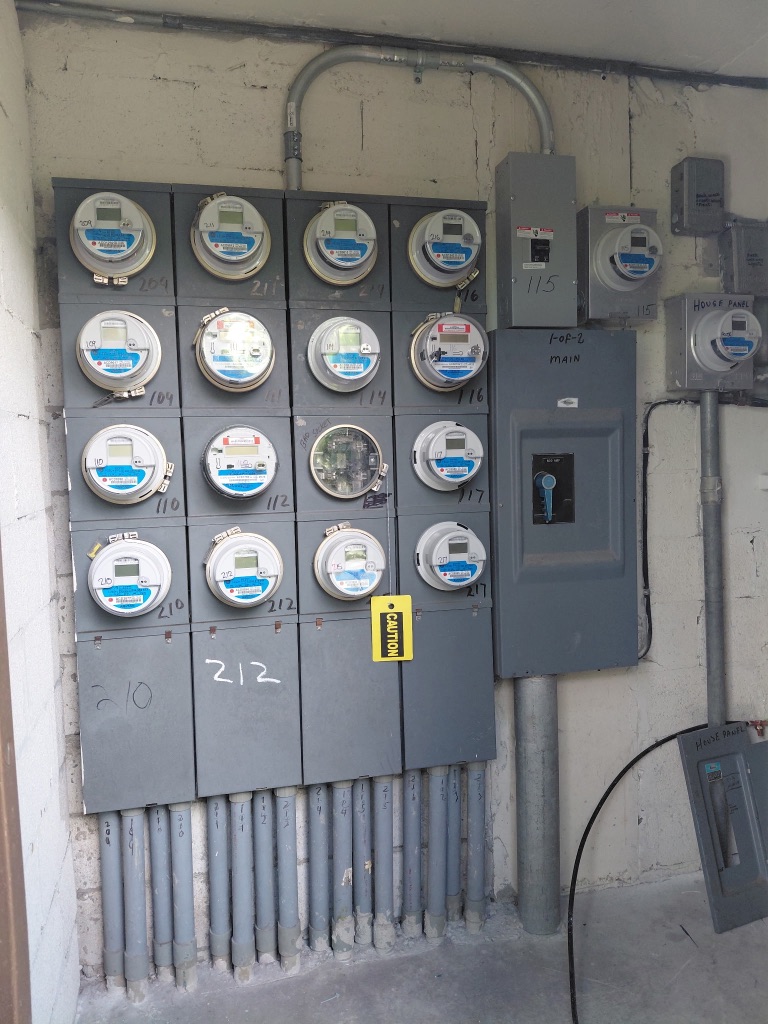 Install 2 Before — Existing Meter Bank with Chalk-Numbered Units, CAUTION Tag, and Old 1-OF-2 MAIN Disconnect — PSEC